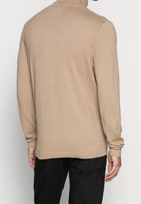Pull beige à manches longues avec un col montant. Confectionné en matière tricotée douce. Présente une coupe ajustée avec des poignets et un bas en côtes.