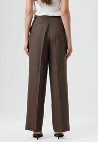 Bruine, wijde broek van een gestructureerde stof, met een taille op middenhoogte en twee achterzakken, gestyled met open-toe hakken.