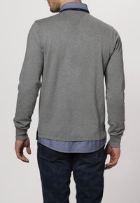 Graues Langarmshirt aus weichem Stoff, mit einem kontrastierenden blauen Kragen, schlanker Passform und geradem Saum mit seitlichen Schlitzen.