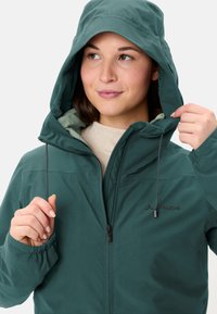 Teal waterdichte jas met capuchon, voorzien van trekkoorden en elastische manchetten. Inclusief een ritssluiting aan de voorkant en een logo op de borst.