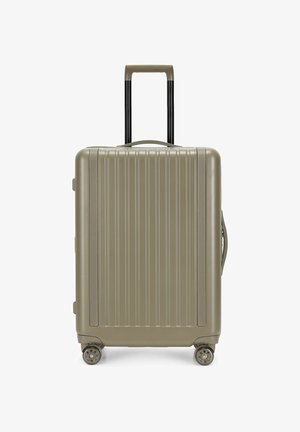 Valigia rigida beige con scanalature verticali, quattro ruote, maniglia retrattile estesa e maniglie laterali e superiori per il trasporto.