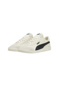 Sneaker in pelle color crema con una striscia laterale in suede nero, suola in gomma texturizzata e lacci tono su tono; presenta il logo Puma sulla linguetta e sul lato.