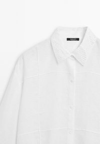 Chemise blanche à manches longues en lin, avec un col brodé détaillé et un motif carré de couture.