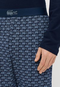 Pantalones de pijama azul marino con estampado, con logotipos blancos de "Lacoste", cinturilla elástica azul marino sólida, tela suave y corte relajado.