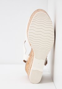 Sandalo bianco con tacco in sughero, suola in gomma texturizzata con un motivo ondulato e un semplice design della cinghia regolabile.