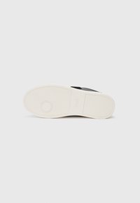 Sandal nero con suola in gomma bianca, caratterizzato da una texture liscia, design minimalista e dettaglio con logo circolare sulla suola.