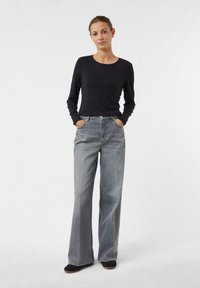 Schwarzes Langarmoberteil mit Perlendetails, kombiniert mit hochgeschnittenen, weiten grauen Jeans. Einfaches Design und lässige Passform.