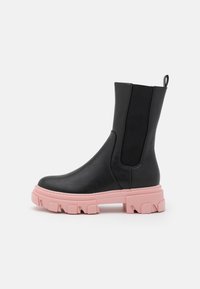 Botín de cuero negro hasta el tobillo con suela gruesa rosa, paneles laterales elásticos y una lengüeta para facilitar el calzado. Textura suave, diseño moderno, material duradero.