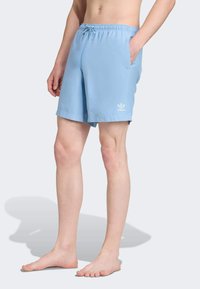 Světle modré plavky z nylonu s elastickým pasem a šňůrkou, dvěma bočními kapsami a bílým logem.