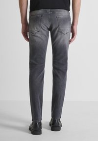 Jeans de mezclilla de corte slim en gris oscuro con un acabado desgastado. Cuenta con dos bolsillos traseros y detalles de costura sutiles. Se llevan con botas negras de tobillo.