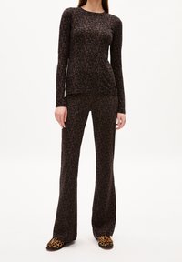 Schwarzes Langarmoberteil und weit geschnittene Hose mit pinkfarbigem Blumenmuster, aus weichem Stoff. Das Modell trägt Hausschuhe mit Leopardenmuster.