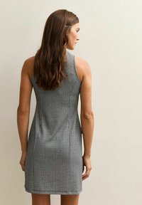 Abito senza maniche a scacchi bianco e nero con un design aderente, realizzato in tessuto testurizzato e con orlo lungo fino a metà coscia sul retro.