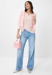 Helles rosa Oberteil mit einem Schlüssellochdesign, getragen unter einer passenden Strickjacke. Hellblaue weit geschnittene Jeans und silberne spitz zulaufende Ballerinas. Pinke Handtasche.