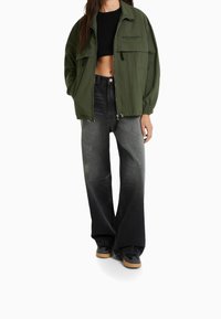 Zielona, oversize'owa kurtka o luźnym fasonie, połączona z wysokim stanem, wyblakłymi czarnymi jeansami i czarnymi sneakersami z beżową podeszwą.