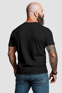 Black short-sleeve t-shirt, cotton material, fitted shape, smooth texture, worn with blue denim jeans, showing tattoos on the forearm.