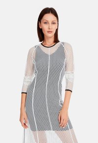 Langärmliges Kleid aus transparentem schwarzem Netz mit weißen Punkten, mit einem runden Ausschnitt und schlanker Passform, akzentuiert mit festen schwarzen Besätzen.