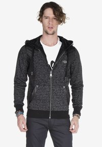 Schwarz-grauer Zip-Hoodie mit strukturiertem Stoff, gesteppten Lederakzenten an den Schultern, Fronttaschen und einer Kapuze mit Zugband.