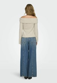 Jersey de canalé beige con hombros al aire, combinado con jeans de mezclilla azul de pierna ancha. Las botas tienen un tacón grueso y una superficie texturizada.