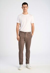 Bruine slim-fit broek met zijzakken, een knoopsluiting en omgeslagen pijpen, gecombineerd met een effen witte t-shirt met korte mouwen en witte sneakers.
