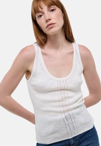 Débardeur en tricot blanc avec un col rond, présentant un motif vertical texturé et un ourlet côtelé. Tissu doux et léger.