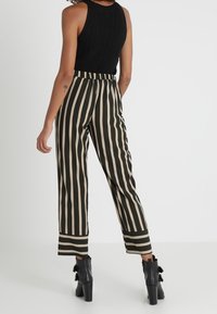 Pantalon rayé noir et beige avec une ceinture élastique, des jambes fuselées et une longueur raccourcie. Porté avec des bottines noires.