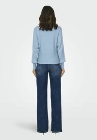 Light blue ribbed sweater with balloon sleeves, paired with dark blue wide-leg denim jeans. Sweater has a cropped hem and textured finish.