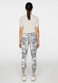 Leggings bianchi con stampa leopardata nera, abbinati a una maglietta beige. I leggings presentano un design aderente e un materiale elastico.