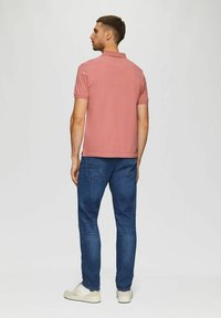 Rosa Poloshirt mit kurzen Ärmeln, kombiniert mit blauen Jeans und weißen Sneakers. Das Shirt hat einen klassischen Kragen und eine glatte Textur.