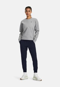 Gray sweatshirt with ribbed cuffs and hem, worn with navy joggers. Model stands with hands in pockets, white sneakers visible.