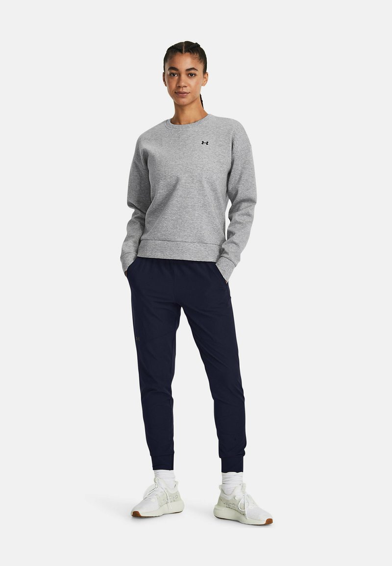 Gray sweatshirt with ribbed cuffs and hem, worn with navy joggers. Model stands with hands in pockets, white sneakers visible.