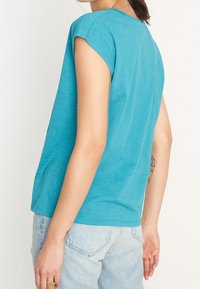 Tričko s krátkým rukávem a kulatým výstřihem v tyrkysově modré barvě, vyrobené z jemné bavlny, s uvolněným střihem a hladkou texturou bez viditelných vzorů.