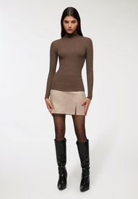 Maglione a collo alto a coste marrone abbinato a una mini gonna beige con uno spacco frontale. Gli stivali neri alti fino al ginocchio con tacco completano l'outfit.
