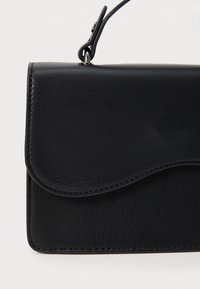 Sac à main en cuir noir avec une fermeture à rabat, bords arrondis et détails de couture. Dispose d'une poignée solide et d'une texture lisse.
