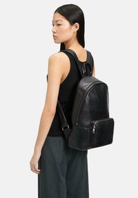 Czarny skórzany plecak o smukłym designie, z główną kieszenią na zamek i przednią kieszenią na zamek do dodatkowego przechowywania.