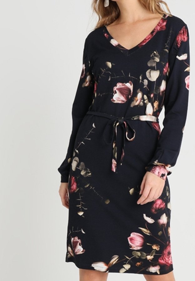 Kwiatowa sukienka uszyta z granatowego materiału, z dekoltem w kształcie litery V, długimi rękawami, paskiem w talii oraz wzorem różowych i kremowych kwiatów z zielonymi akcentami.