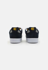 Navy suede sneakers with white rubber soles, gray accents, and yellow branding on the heel. Rounded shape with low top cut.