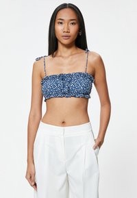 Top corto de color azul marino con patrón floral blanco, bordes con volantes y tirantes ajustables. Combinado con pantalones blancos de cintura alta.