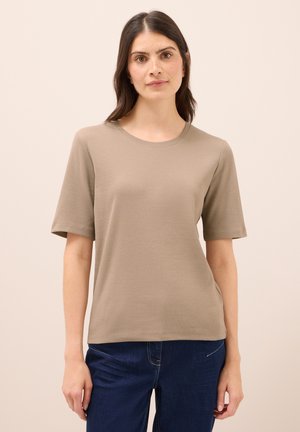 Beżowy t-shirt z krótkim rękawem, okrągłym dekoltem i prążkowaną fakturą. Gładki materiał; noszony z ciemnoniebieskimi dżinsami.