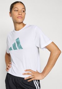 Valge lühikeste varrukatega spordisärk, mille esiküljel on teemandivärvi triibuline logo. Särk on valmistatud kergest ja hingavast materjalist. Mudelil on seljas mustad lühikesed püksid.