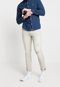 Laivastonsininen napillinen paita, jossa on teksturoitu kuvio, yhdistetty vaaleanbeigeihin kuluneisiin farkkuihin ja valkoisiin tennareihin.