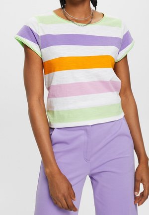 Persoon draagt een korte mouw gestreept shirt met paarse, oranje, groene en witte kleuren en lichtpaarse broek, accessorized met zilveren kettingen.