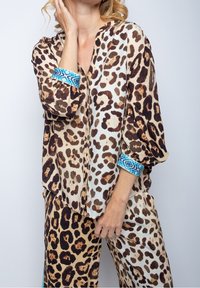Blusa con stampa leopardata in tessuto leggero, caratterizzata da polsini a fantasia blu e una vestibilità morbida. Il design include varie tonalità di marrone e beige.