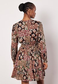 Vestido con estampado floral fabricado en un tejido ligero. Presenta mangas largas, una cintura fruncida y una falda fluida con dobladillo acampanado. Los colores predominantes son el negro, burdeos y verde.