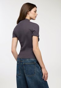 Dopasowany fioletowy prążkowany top z krótkimi rękawami, zestawiony z wysokim stanem niebieskimi dżinsami o szerokich nogawkach z dwiema tylne kieszeniami.