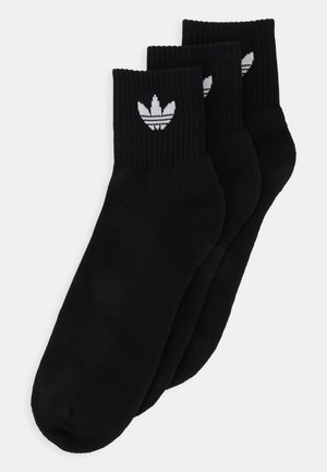 Černé kotníkové ponožky z bavlny, s žebrovanou strukturou, obsahující bílé logo trefoil Adidas na lemu. Balení obsahuje tři páry.