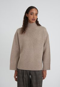 Maglione beige lavorato a maglia con colletto alto a coste, spalle scese e polsini a coste. Abbinato a pantaloni a gamba larga grigi a fantasia quadri.