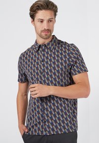 Camisa de manga corta con un patrón geométrico en colores azul, marrón y crema. Con cuello y cierre de botones, está confeccionada en tejido ligero.