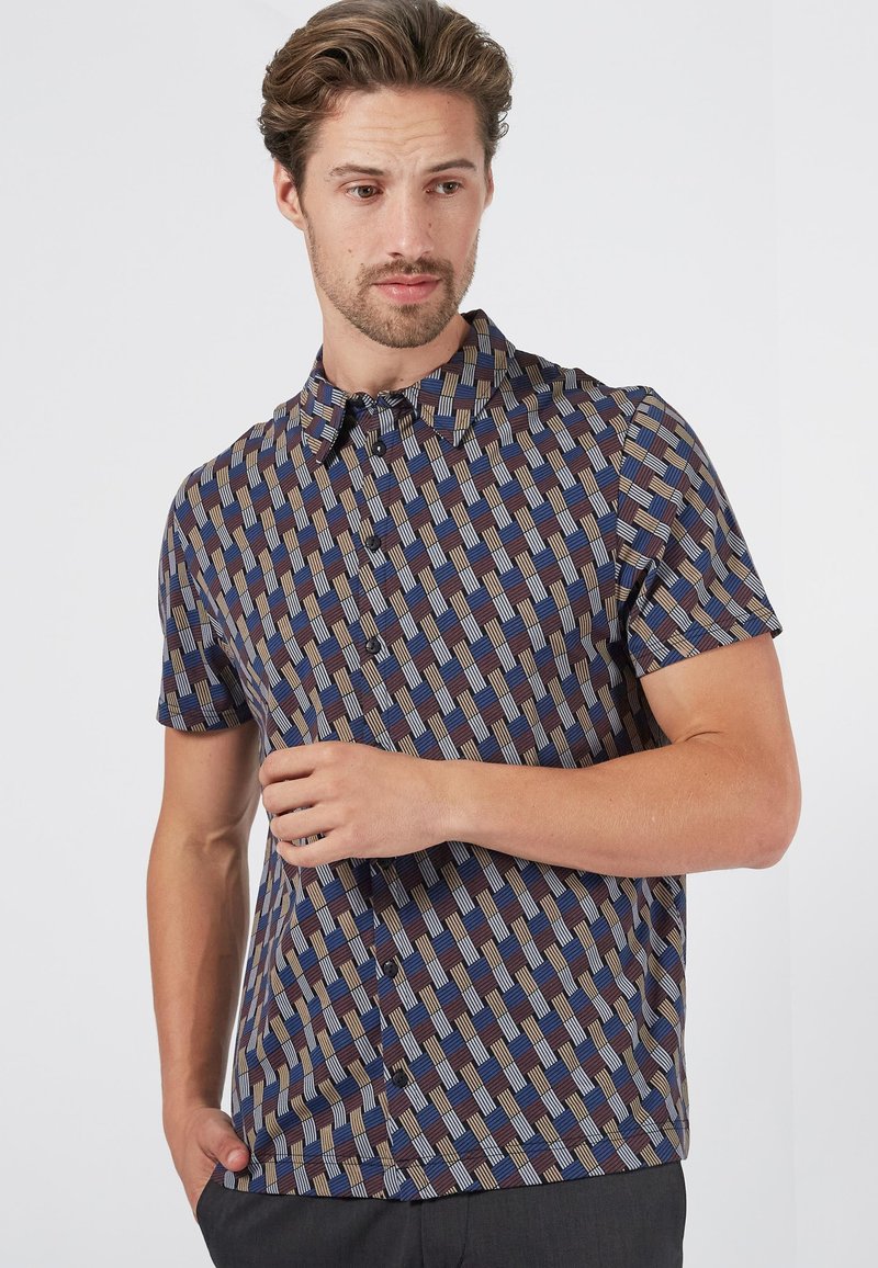 Camisa de manga corta con un patrón geométrico en colores azul, marrón y crema. Con cuello y cierre de botones, está confeccionada en tejido ligero.