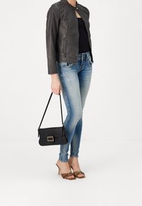 Svart läderhandväska med rektangulär form och guldfärgad hårdvara, kombinerad med mörka jeans och bruna sandaler med klack och nitar.