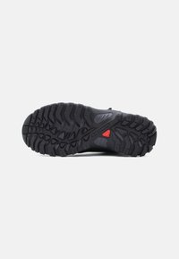 Melnas sneakers zoles ar izteiktu protektora rakstu, sarkanu akcentu un zīmola logotipu. Materiāls izskatās izturīgs ar dažādām faktūrām, kas nodrošina labāku saķeri.